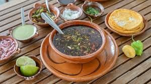 Birria de la 30 consomé with tortillas and salsas served in traditional clay bowls